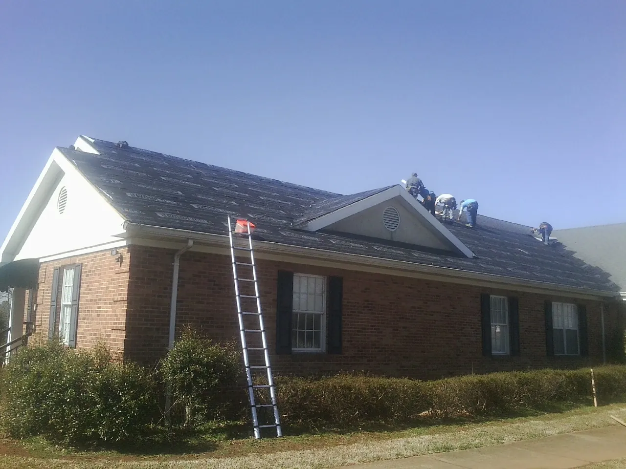Crew tearing shingles off a brick ranch roof with a ladder set — Emergency Roof Repair work by our crew in Dubois