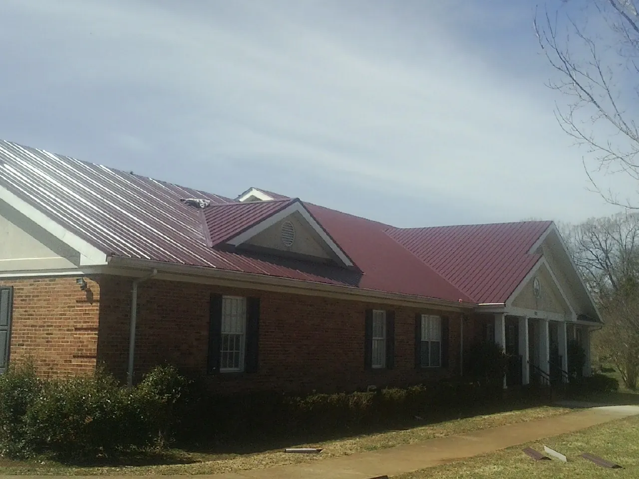 Red metal roof with gabled entries on a long brick building, from a Hail Damage Roof Repair job in Dubois