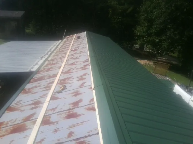 Old rusted panels beside newly installed green metal roofing — Wind Damage Roof Repair by Roofing Brothers in Dubois