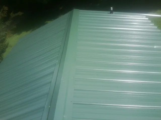 New green metal panels meeting at the ridge of a roof — Flat Roof Repair work by our crew in Dubois