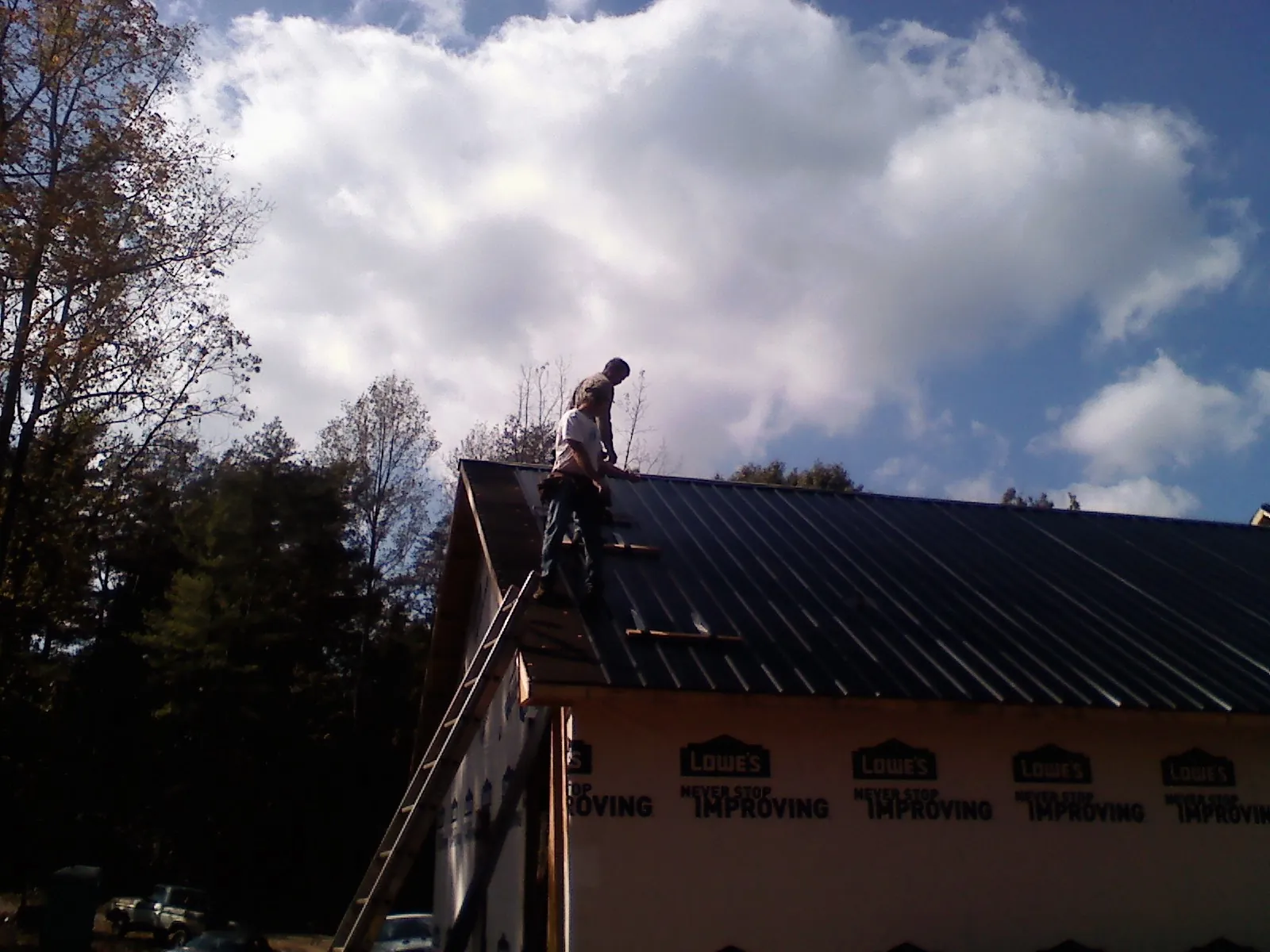 Roofer fastening dark metal panels high against a cloudy sky, from a Roof Inspection job in Dubois