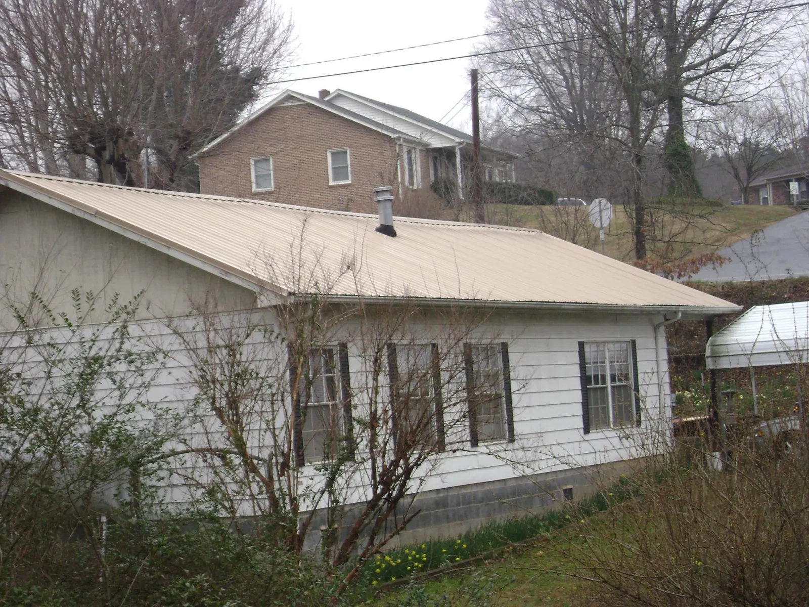 Tan metal roof on a white sided house set into a hillside — Commercial Roofing by Roofing Brothers in Dubois