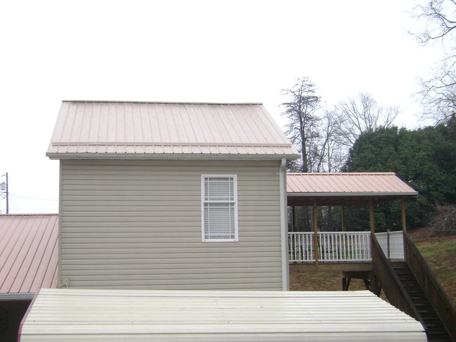 Tan metal roofs on a two story addition and attached porch, from a Roof Replacement job in Dubois